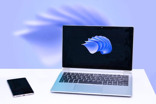 Modern white office work table or desk with portable laptop computer with abstract background and smartphone with blank screen over abstract technology background.