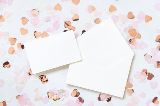 Horizontal card and envelope between pink hearts on white table top view. Romantic mockup for Wedding, Valentines, Spring or Mothers day