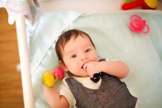 baby,lying,awake,crib,top view,white skin,suit,toys