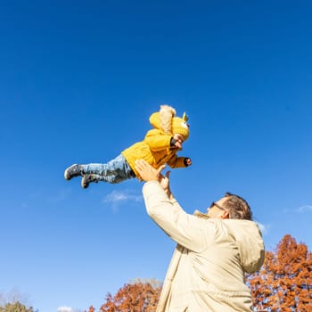 More, more,... dad, that's fun. Happy young father throws his cute little baby boy up in the air. Father's Day, Father and his son baby boy playing and hugging outdoors in nature in fall
