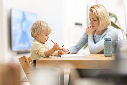 Caring young Caucasian mother and small son drawing painting in notebook at home together. Loving mom or nanny having fun learning and playing with her little 1,5 year old infant baby boy child
