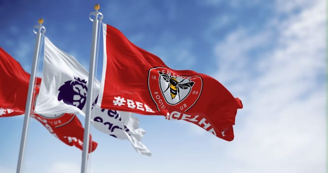 London, UK, Dec 19 2023: Brentford Football Club and Premier League flags waving in the wind on a clear day. Circular emblem with a bee inside on red. Illustrative editorial 3d illustration render