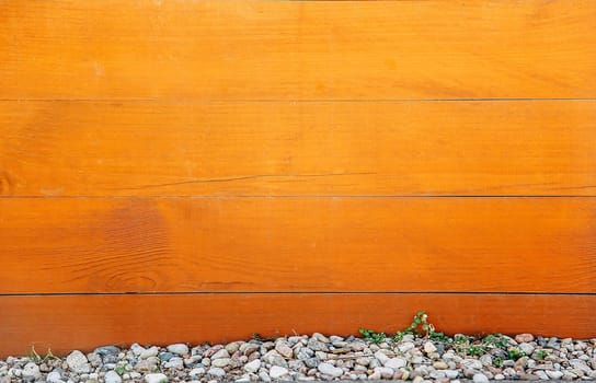 A horizontal wooden board of brown color with knots on the surface and small stones at the bottom.Texture or background