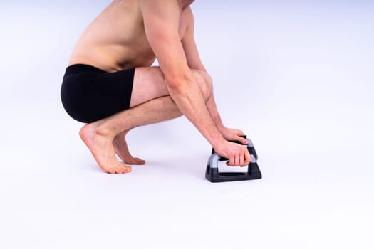Shirtless muscular athlete do push-up on push up bars. Full body man on white studio background.