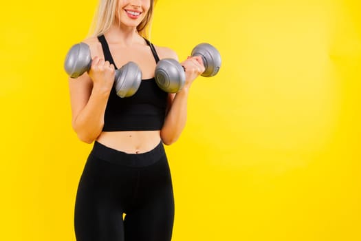 Athletic woman in a sportswear raises dumbbells leads healthy lifestyle has happy expression