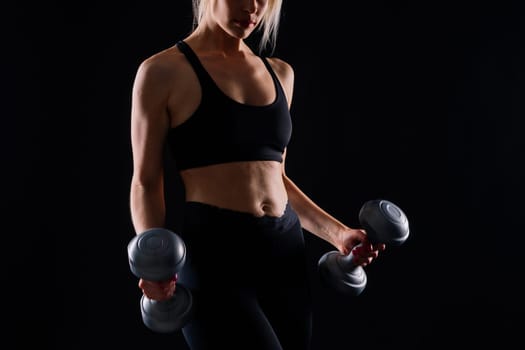 Athletic woman in a sportswear raises dumbbells leads healthy lifestyle has happy expression