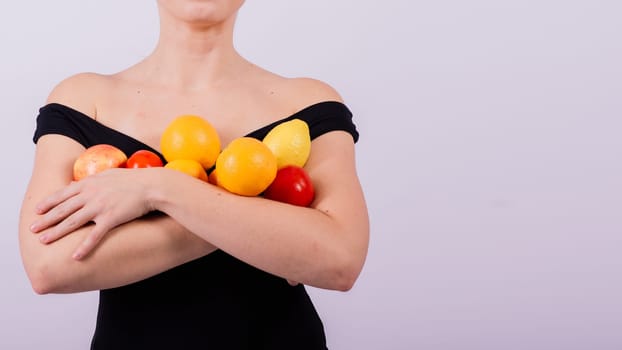 A female holding an apples, lemons, oranges in different arms isolated on grey background.
