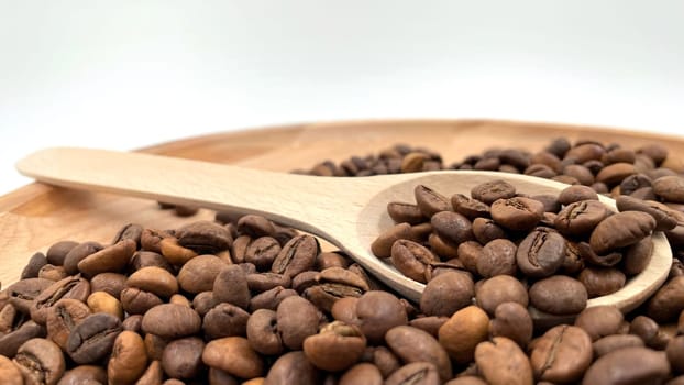 Food background texture of roasted coffee beans with a full shovel. A pile of scattered aromatic roasted brown coffee beans with a wooden scoop. Coffee beans in a wooden spoon