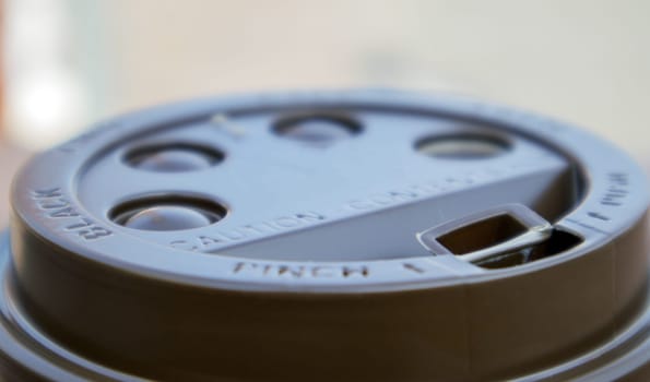 Brown plastic lid on a paper coffee cup close-up. Takeaway cup for drinks. Breakfast, coffee time. Drinks and cafe concept