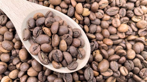 Food background texture of roasted coffee beans with a full shovel. A pile of scattered aromatic roasted brown coffee beans with a wooden scoop. Coffee beans in a wooden spoon