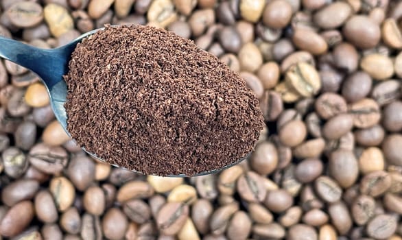 Ground coffee powder in a metal spoon in the foreground, against the background of roasted aromatic coffee beans. Coffee concept