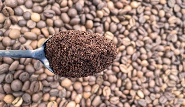 Ground coffee powder in a metal spoon in the foreground, against the background of roasted aromatic coffee beans. Coffee concept