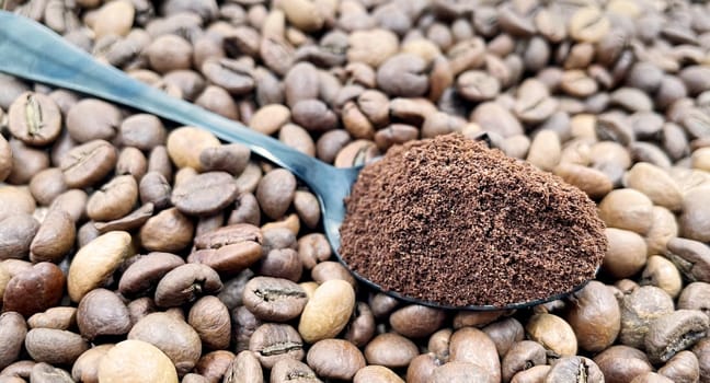 Ground coffee powder in a metal spoon in the foreground, against the background of roasted aromatic coffee beans. Coffee concept