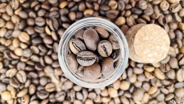 Coffee beans in a small glass jar with a cork lid on the table. Coffee beans packed in a transparent, airtight storage container. Coffee seeds inside a glass jar. Flat layout