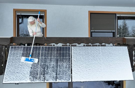 A woman removes snow from a balcony power station in winter