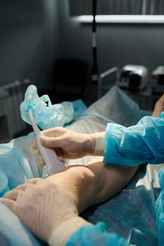 Hands of male surgeon in protective rubber gloves holding probe close to knee of young female patient lying on operation table