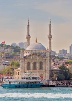 Istanbul, Turkey - May 8 2023: View from Bosphorus Strait overlooking Ortakoy Mosque, or Ortakoy Camii, aka Buyuk Mecidiye Camii with a ferry boat in front before sunset, suited at Ortakoy pier square