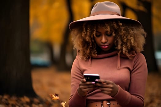 curly blonde African American young adult woman with a hat sitting on the ground in fallen autumn maple leaves looking in her cellphone. AI generated image. Not based on any actual person or scene.
