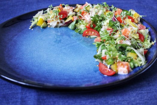 Salad of fresh vegetables on a plate on a blue background, a close-up view from an angle