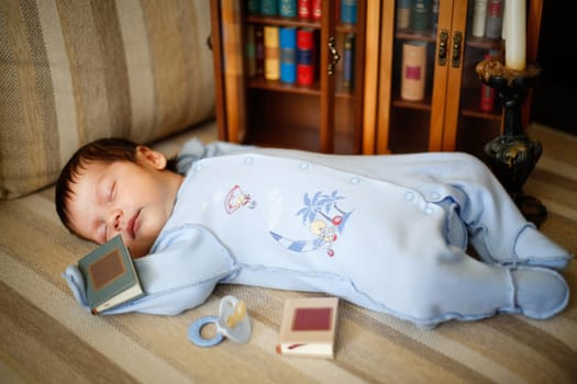 A little kid fell asleep on the couch next to books and a pacifier close-up view from an angle
