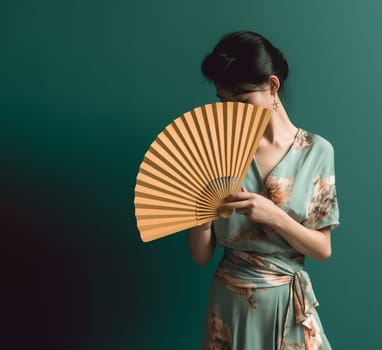 Woman in floral kimono with fan against teal backdrop.
