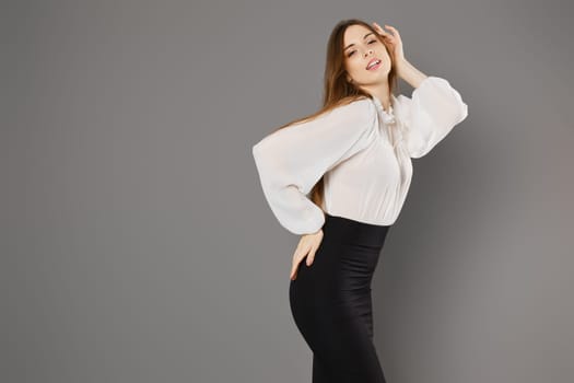 Gorgeous young woman in pencil skirt and blouse posing in grey studio