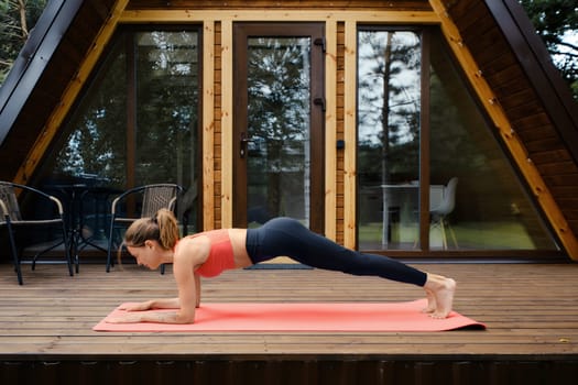 Woman in sportswear does plank exercise on the porch of a-frame cabin