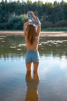 Unrecognizable young woman enters the river and taking her shirt off