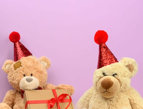 Sad teddy beige bear in a red cap sits on a purple background