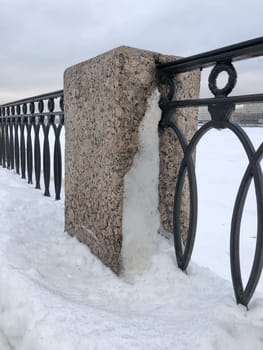 granite pillar and cast iron embankment fence in the snow, winter landscape St. Petersburg