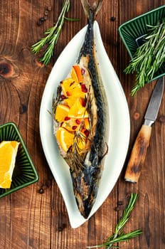 Mackerel fish baked with oranges and rosemary on a vintage wooden background.
