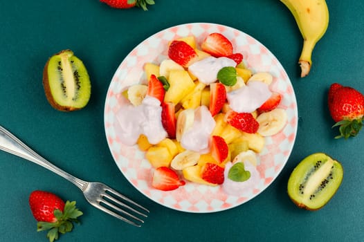 Delicious fruit salad of strawberries, pineapple, kiwi and yogurt on old rustic wooden table.