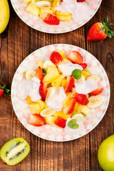 Delicious fruit salad of strawberries, pineapple, kiwi and yogurt on old rustic wooden table.