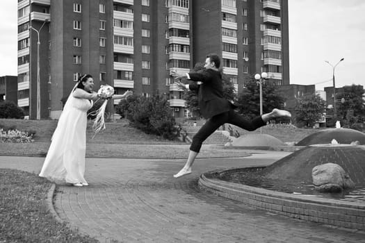 The groom jumps barefoot over the fountain to the bride on the street in the afternoon. Monochrome photography