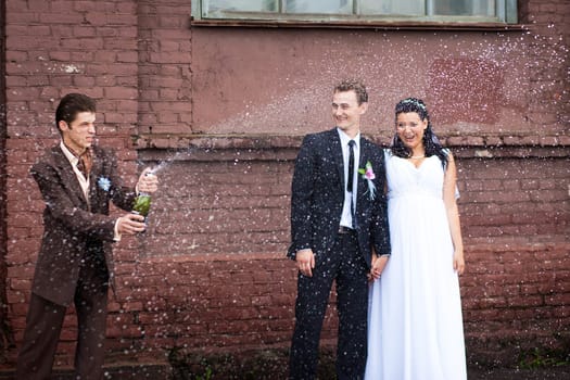 A witness on the street opened champagne with splashes on the background of the bride and groom