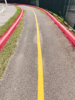 Deserted asphalt cycle path. Demarcated in red and yellow with a curve in perspective on a sunny day.