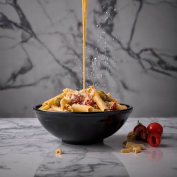 Italian pasta mixed with vegetables, pouring in bowl. Delicious