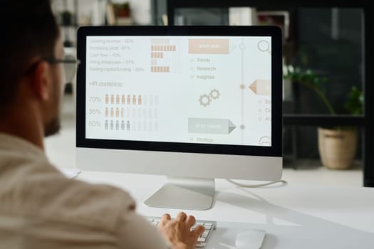 Screen of desktop computer with statistic data standing on workplace of young analyst or manager typing on keyboard during work