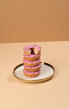 Donut covered with pink glaze and sprinkled with colorful sprinkles on a round plate, brown background