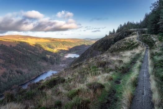 Wooden boardwalk on the top of a mountain with scenic view on Glendalough lakes and forest. Hiking in beautiful autumn Wicklow Mountains, Ireland