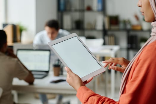 Tablet with blank screen in hands of young Muslim female manager standing in front of camera in coworking space