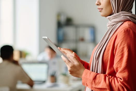 Cropped shot of young Muslim female manager using tablet while standing in coworking space against male colleagues