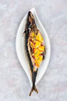 Whole mackerel fish baked with oranges and rosemary served on a stylish plate.