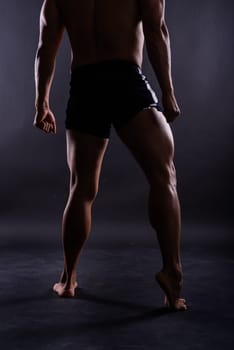Muscular male legs, man in a studio, dark background