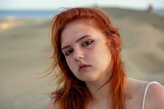 Young girl with red hair, on the beach in summer, her hair tousled by the wind