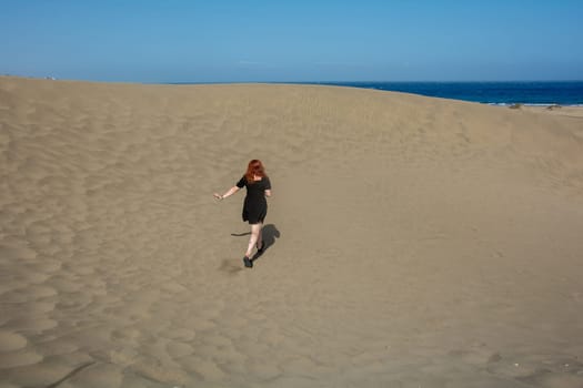 Young woman running up a sand dune towards the sea, with blue sky