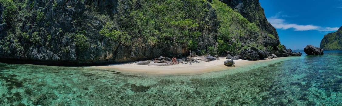 Panoramic view of a couple enjoying island hopping on a tropical Secret beach in Matinloc island, Philippines.