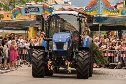 Villach, Austria - August 6, 2022: A tractor joins the procession of 'Villacher Kirchtag', the largest traditional folk festival in Austria, after some years of cancellation due to Covid.