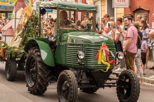 Villach, Austria - August 6, 2022: A tractor joins the procession of 'Villacher Kirchtag', the largest traditional folk festival in Austria, after some years of cancellation due to Covid.