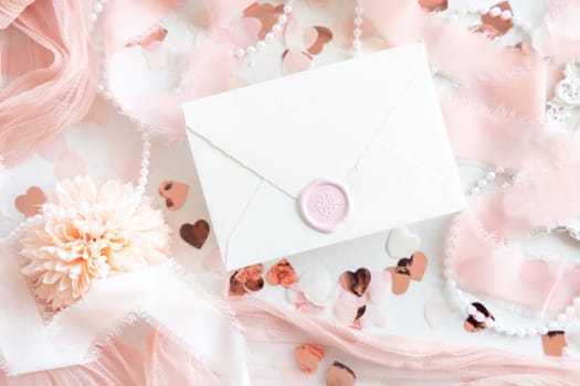 Sealed envelope near pink decorations, hearts and silk ribbons on white table top view, mockup. Romantic scene with vertical blank card flat lay. Wedding, Valentines, Spring or Mothers day stationery